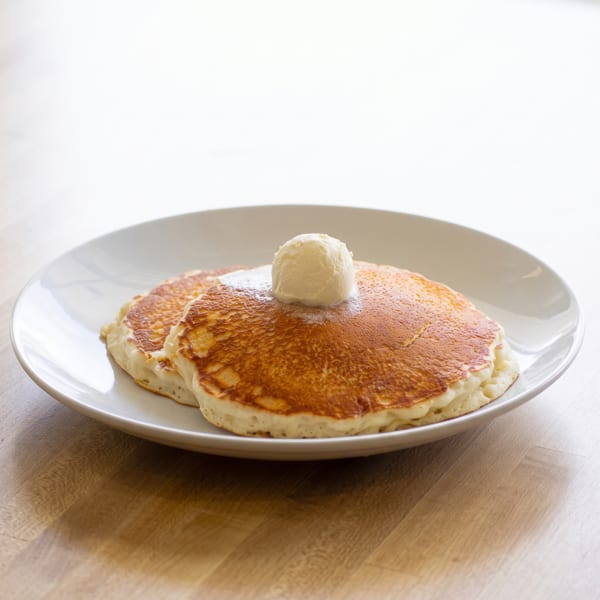 Two golden pancakes with a scoop of melting vanilla ice cream on a white plate.