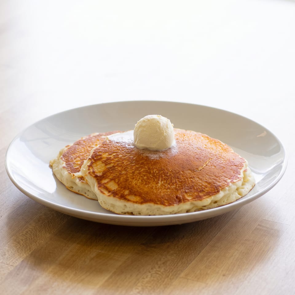 Two golden pancakes with a scoop of melting vanilla ice cream on a white plate.