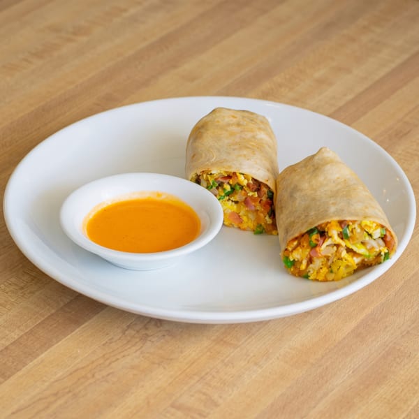 Two breakfast burritos filled with eggs, potatoes, and vegetables, served with orange dipping sauce.