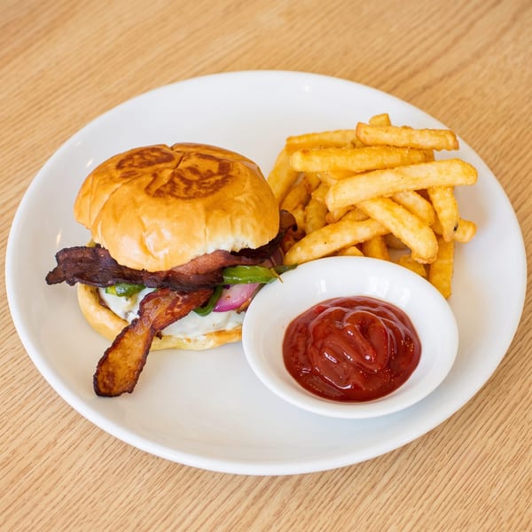 A bacon cheeseburger with red onion and green peppers, served with fries and ketchup on a white plate.